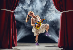 Cute little child girl playing guitar on stage. Kid dreams of be